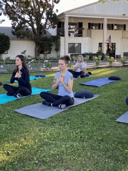 Clients in guided outdoor meditation on the lawn at Northbound's Garden Grove campus — somatic yoga and mindfulness as part of the Spiritual Track