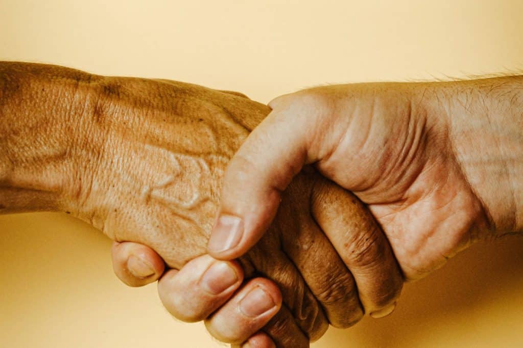 Two men shake hands with a yellow background as they discuss the financial benefits of insurance for drug rehab programs.