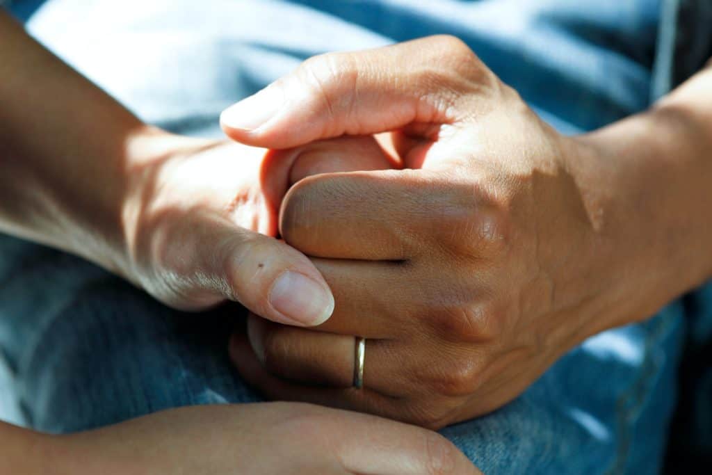 An up-close view of two individuals grasping each other’s hands as they discuss the benefits of a residential treatment facility.
