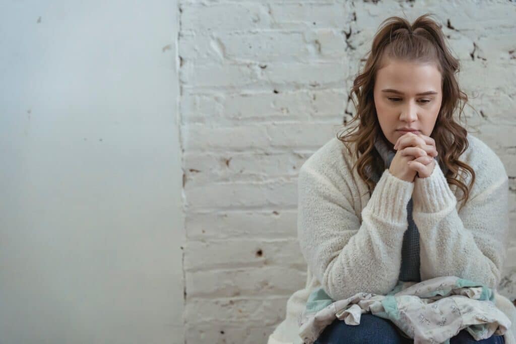 A woman deep in consideration sitting against white brick wall.