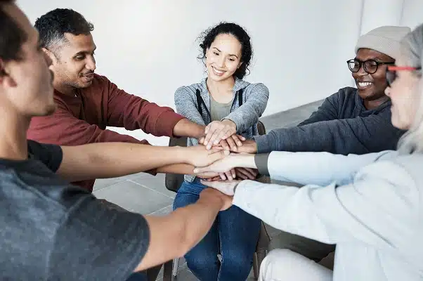 People in a recovery group sitting in a circle, hands stacked together, symbolizing support and hope